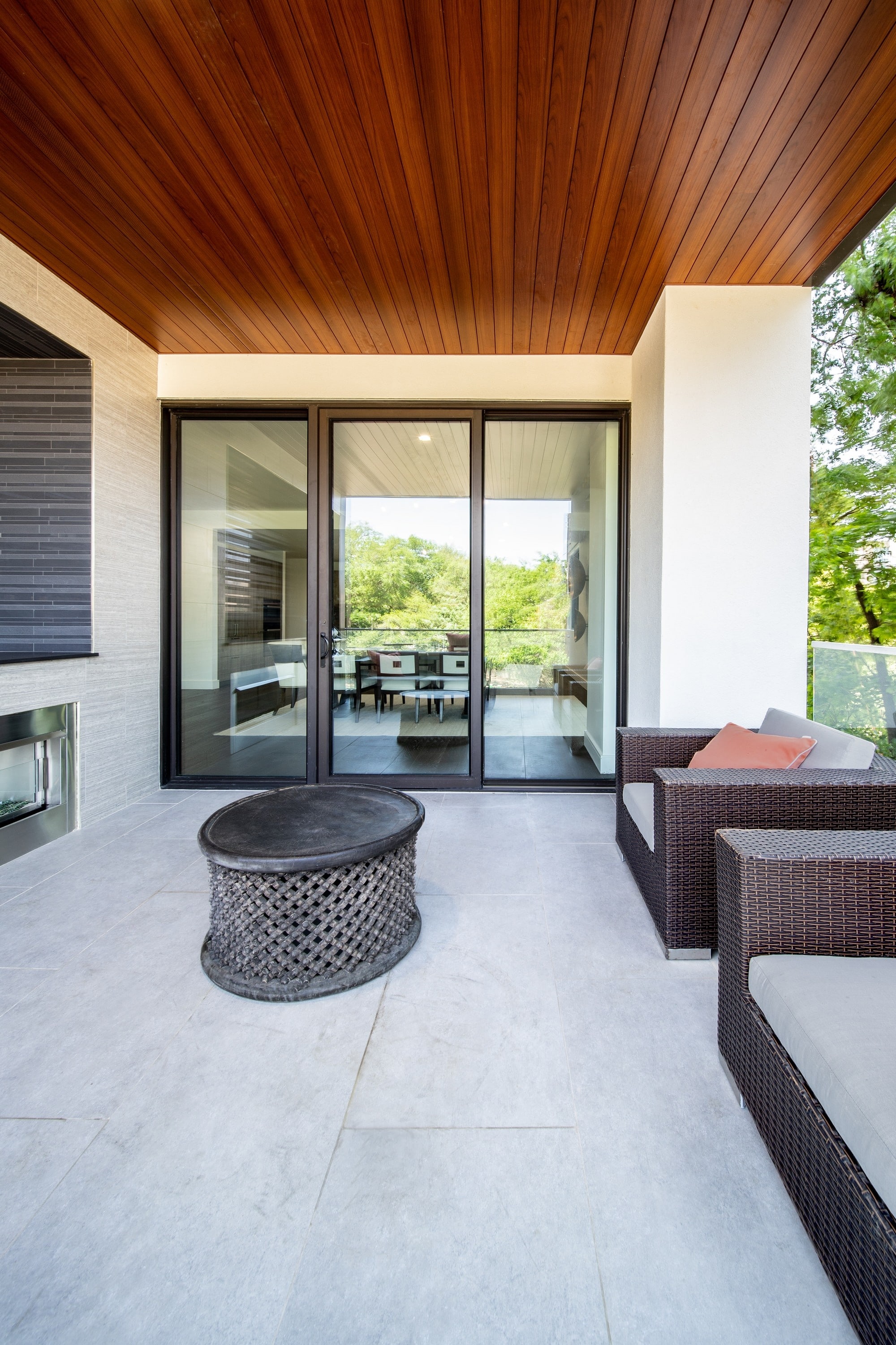 Modern Alfresco Aluminium sliding door with sidelight in nightsky colour,outdoor furniture to the fore and timber sheeted ceiling.